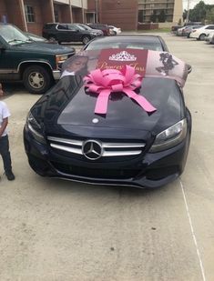 a young boy standing next to a black car with a pink bow on it