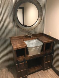 a bathroom with a round mirror above the sink and wooden cabinet below it, along with a trash can