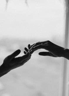 two hands reaching out towards each other in front of a window with the ocean outside