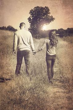 a man and woman holding hands while walking through a field