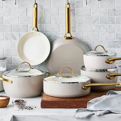 white pots and pans with gold handles sitting on a counter