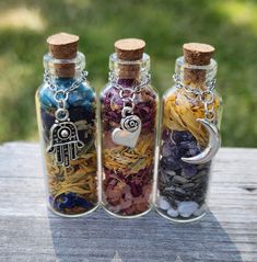 three glass bottles filled with different types of beads and charms sitting on top of a wooden table