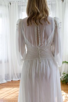 the back of a woman's white dress in front of a window with curtains