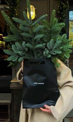 a woman holding a black shopping bag in front of a christmas tree