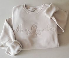 The perfect gift for a bride to be! Personalize this crewneck with the Brides new last name the wedding year!  Snuggle up in the coziest sweatshirt ever! This sweatshirt is so buttery soft and lightweight so it is perfect to wear year round. It's not super thick giving it a nice light weight feel.  This crewneck is perfect for the bride to get ready in the day of her wedding! Pair with our single initial crewnecks for the bridal party to wear!  TO ADD EXTRA EMBROIDERY TO SLEEVE CUFF: https://www Embroidery Names On Sweatshirts, Custom Name White Crew Neck Sweatshirt, White Custom Embroidered Sweatshirt, Bridal Party Crew Neck Sweatshirt, Embroidered Mrs Sweatshirt, Swimwear Boutique, Comfort Colors Tshirt, Embroidered Crewneck, Embroidery Monogram