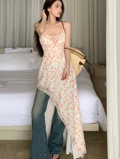 a woman standing in front of a bed wearing jeans and a tank top with flowers on it