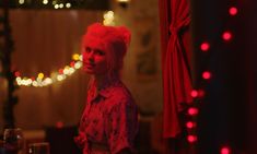 a woman with pink hair standing in front of a christmas tree and decorated with lights