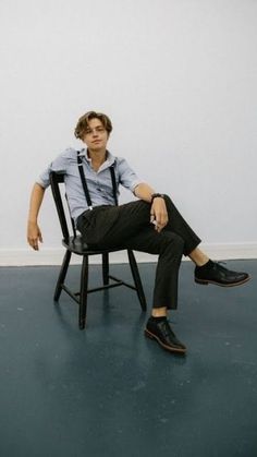 a young man sitting in a chair with his legs crossed and one foot on the ground