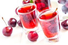 three glasses filled with red liquid and cherries on a white tablecloth stock photo