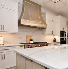 a kitchen with white cabinets and marble counter tops, gold trimming on the hood