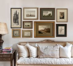 a living room filled with lots of framed pictures on the wall above a white couch