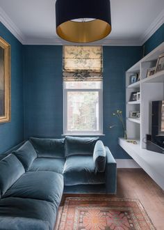 a living room with blue walls and a large couch in front of a window that has a rug on the floor