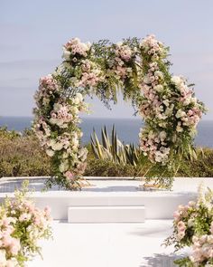 an outdoor ceremony setup with flowers and greenery on the ground, overlooking the ocean