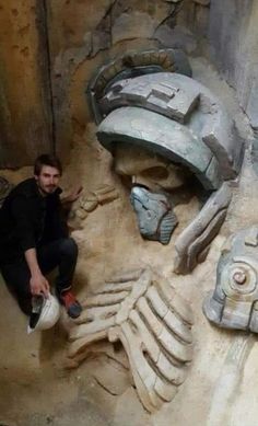 a man kneeling down next to a statue of a human head and hands on the ground