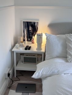 a bed with white sheets and pillows next to a table with an electronic device on it