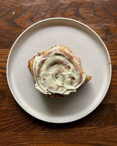 a white plate topped with a pastry covered in icing on top of a wooden table