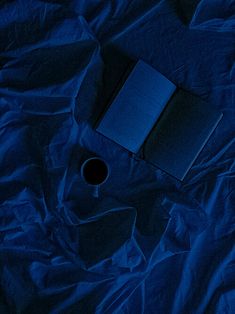 an open book sitting on top of a blue sheet next to a coffee cup and pen