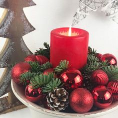 a red candle sitting on top of a bowl filled with ornaments