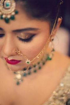 a woman in a gold outfit with green jewels on her head and red lips wearing a necklace