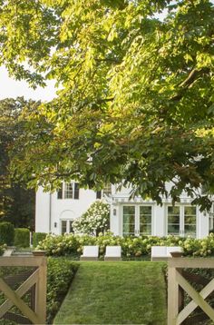 a large white house sitting next to a lush green park filled with trees and bushes