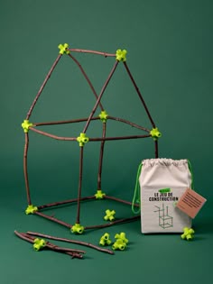 a small building made out of sticks and twigs with a bag next to it on a green background