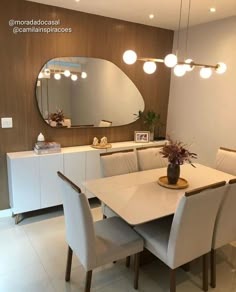 a dining room table with white chairs and a large round mirror on the wall above it