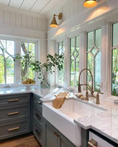 a large kitchen with marble counter tops and gray cabinets, along with two windows that look out onto the trees outside