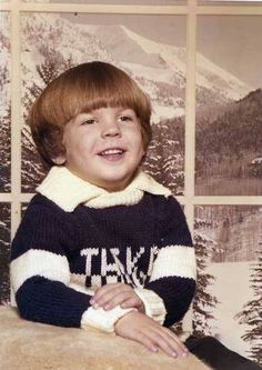 a young boy sitting in front of a window with his hands on his knees and smiling