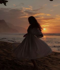 a woman standing on top of a sandy beach next to the ocean at sun set