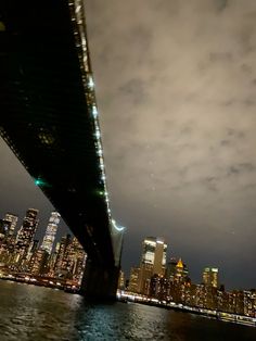 the city skyline is lit up at night as seen from across the water under a bridge