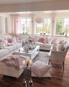 a living room filled with lots of white furniture and pink pillows on the couches