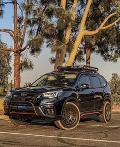 a black subarunt is parked in a parking lot next to some tall trees