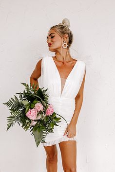 a woman in a short white dress holding a flower bouquet and posing for the camera