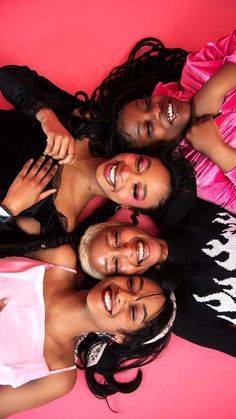 three women are smiling and posing for a photo together on a pink background with one woman in the middle