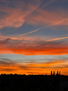 an orange and blue sky with some clouds in the foreground, buildings in the background