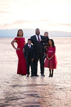 a family poses for a photo in front of the water at sunset with their two children