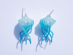 there are two jellyfish shaped earrings on the white surface, one is blue and the other is green