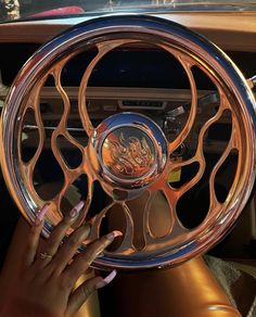 a woman's hand on the steering wheel of a car with chrome spokes