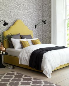 a bed with yellow headboard and pillows in a bedroom next to a large window