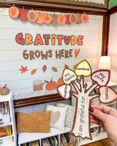 a person holding up a family tree sign in front of a bulletin board that says, gratitude grows here