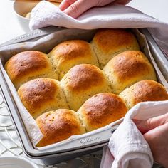 a person holding a baking pan with rolls in it