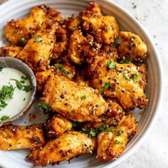 a white plate topped with chicken wings next to a small bowl of ranch dressing on the side