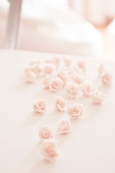 small pink flowers are scattered on a white table top with a blurry bed in the background