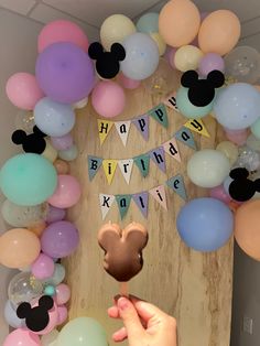 a person holding a cookie in front of a mickey mouse birthday party backdrop with balloons