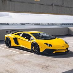 a yellow sports car parked in a parking lot next to the ocean and bridge overpass