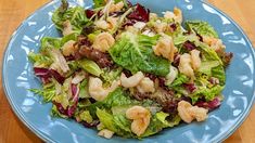 a salad with shrimp and lettuce is on a blue plate, ready to be eaten