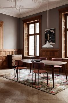 a dining table with four chairs in front of two windows and a rug on the floor