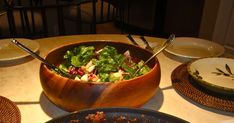 a wooden bowl filled with salad sitting on top of a table next to two plates