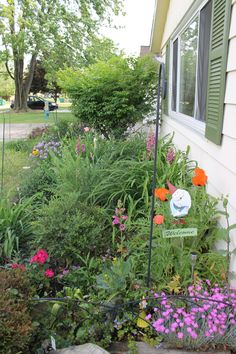 a garden with lots of flowers and plants next to a house that has a sign on it