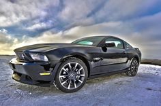 a black car parked on top of a snow covered field next to the ocean and cloudy sky